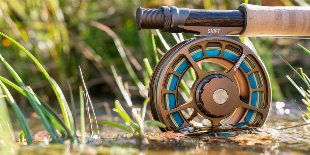 Sage Shift Reel in bronze sitting in shallow water with grass