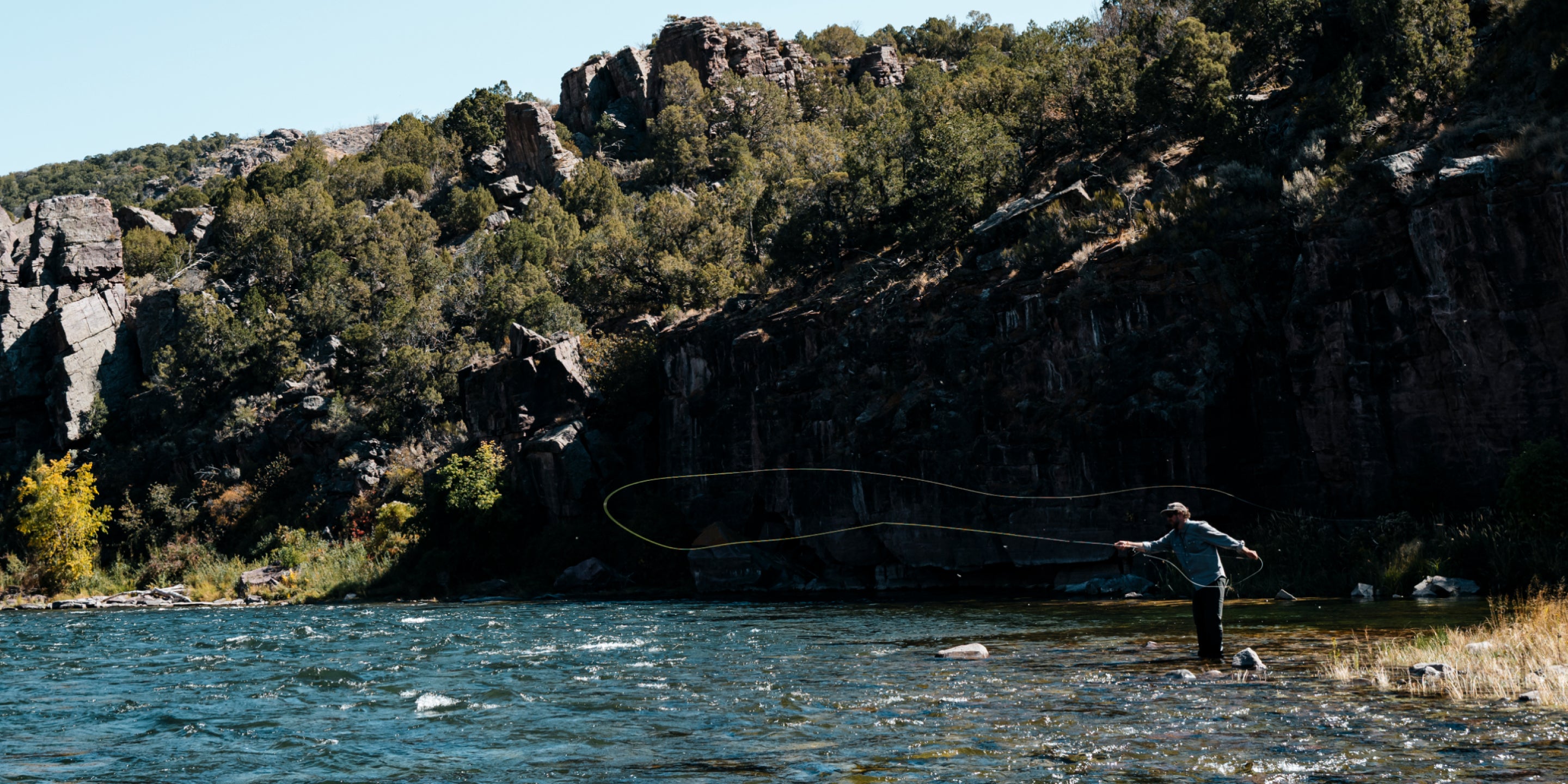 man making long cast on sunny day in front of cliff face